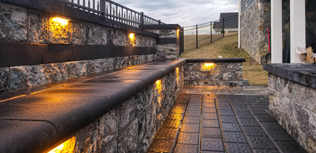 Hardscaped outdoor seating area with illuminated stone walls and a textured stone pathway, highlighting durable materials suitable for freeze-thaw climates.