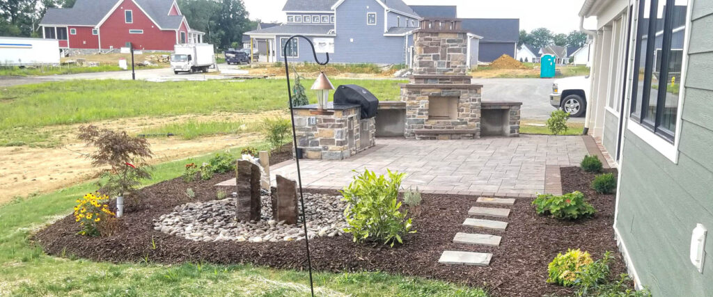 Landscaped patio with stone fireplace, paver walkway, and flower beds, showcasing hardscaping maintenance for seasonal care in Pennsylvania.