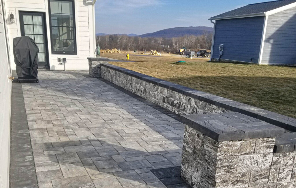 Paved patio area with a stone seating wall, adjacent to a house, showcasing proper hardscaping for seasonal maintenance by ProLawn Landscaping.