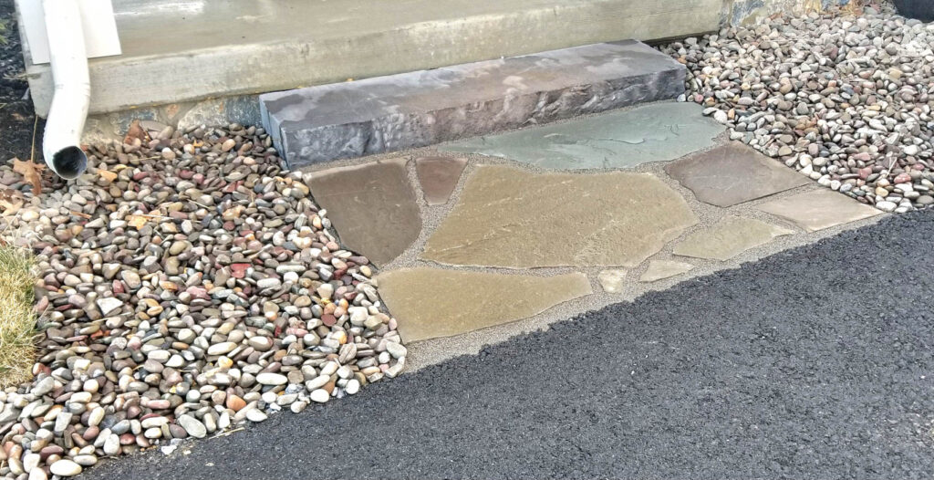 Natural stone walkway with varied flagstone patterns, surrounded by decorative pebbles and compacted gravel, illustrating durable hardscaping solutions for outdoor spaces.