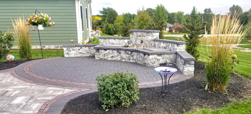 Outdoor hardscaping design featuring a stone patio, seating wall, and ornamental grasses, showcasing space optimization for small yards by ProLawn Landscaping.