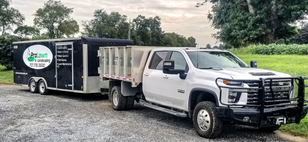 ProLawn Landscaping truck and trailer parked on gravel, ready for leaf cleanup services, showcasing professional equipment for yard maintenance.