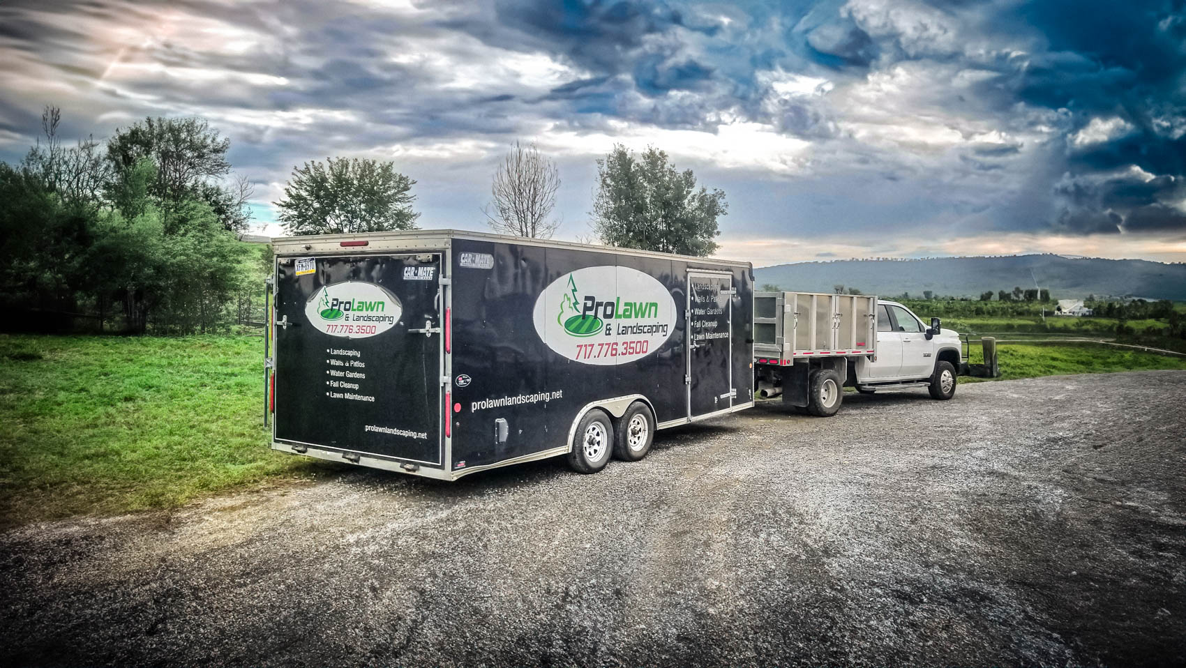 ProLawn Landscaping trailer and truck parked in a scenic outdoor setting, featuring the ProLawn logo and services like landscaping and lawn maintenance, with a cloudy sky and green landscape in the background.