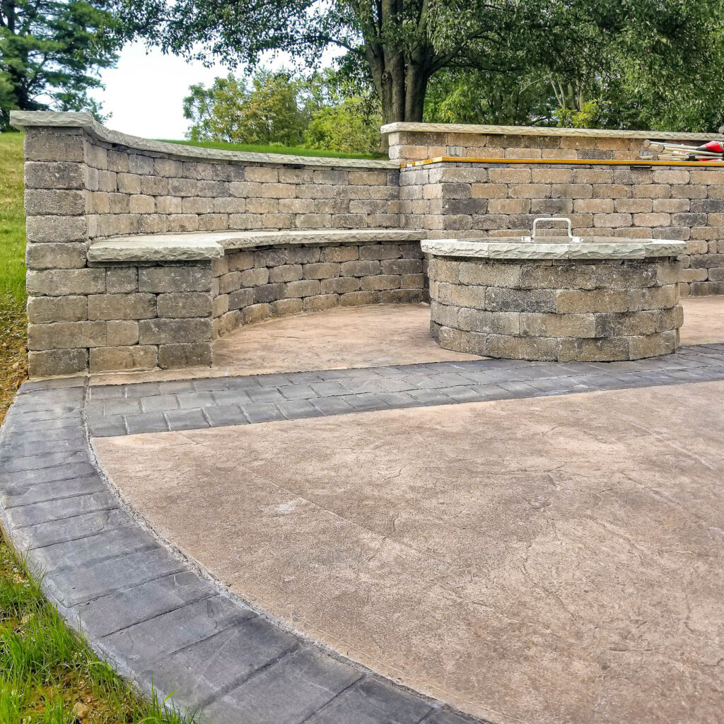 Raised platform patio with curved seating wall and circular stone table, showcasing durable hardscaping materials for small outdoor spaces.
