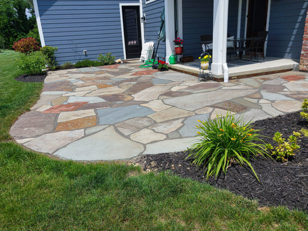 Patio with natural stone pavers, surrounded by green grass and colorful landscaping, illustrating hardscaping maintenance in Pennsylvania.